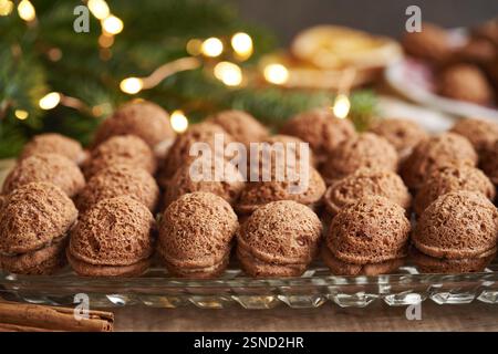 Homemade nut shaped Christmas cookies filled with cocoa cream with fir tree branches and fairy lights in the background Stock Photo