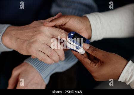 Close up on hand of Black female social worker measuring elderly mans blood oxygen saturation using oximeter during home care visit, image in warm tones Stock Photo