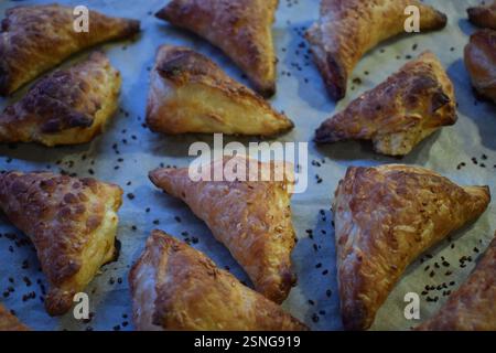 A baking tray filled with freshly baked golden brown triangular cakes. The cakes have a flaky, crunchy texture, are sprinkled with sezam seeds on top. Stock Photo