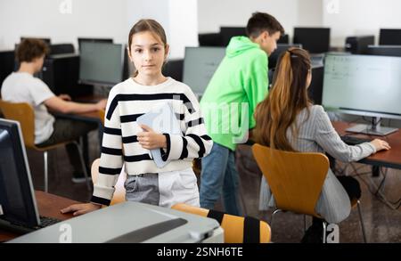 Teen schoolgirl with workbook in hands standing in computer class Stock Photo