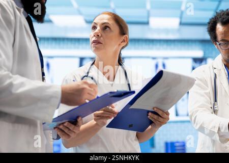 Team of doctors comparing test results and healthcare records in office, consulting experts for disease prevention. Diverse physicians collaborating on finding the right diagnostic in a meeting. Stock Photo