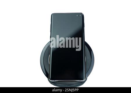 Close-up of a modern black smartphone placed on a wireless charging pad, isolated on a white background, showing technology and convenience. Stock Photo