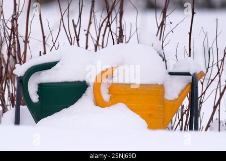 Green and yellow watering cans fully covered with deep snow in winter snowy scene. Stock Photo