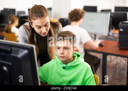 Female teacher consulting tween boy studying in computer class Stock Photo