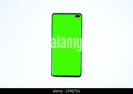 Modern smartphone with a bright green screen placed on a wireless charging pad, isolated on a white background, suitable for mockups and design presen Stock Photo