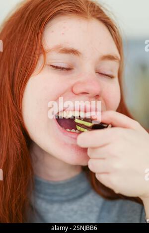 Girl with red hair eating trend Dubai chocolate with pistachio paste and kataifi dough.  Stock Photo