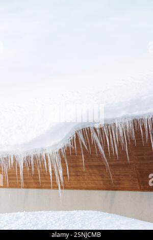 Large icicles hanging from a building roof in covered in white winter snow Stock Photo
