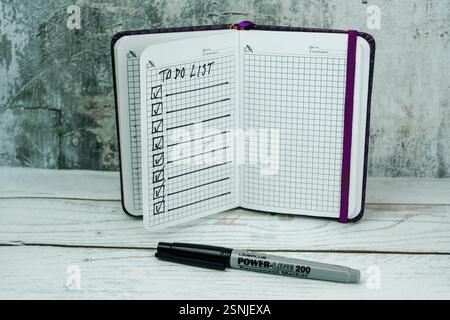 Open notebook with a handwritten to-do list on graph paper, placed on a wooden surface with a gray background. A black marker lies in front of the not Stock Photo