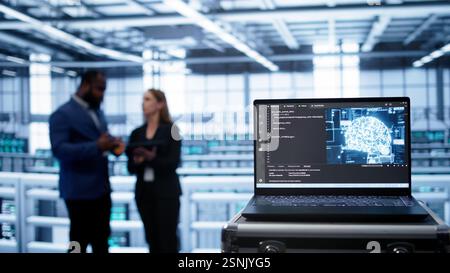 Focus on laptop in data center with artificial intelligence brain used by engineers in blurry background. Close up of device displaying AI deep learning software in server farm, camera B Stock Photo