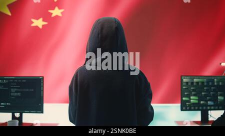 Governmental hacker in high tech office with Chinese flag shown on big screen, IT expert engaged in cyber espionage and criminal activity. Spreading fake news and brainwashing the nation. Camera B. Stock Photo