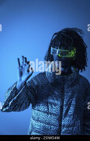 Software engineer wearing futuristic glasses using augmented reality interface making ok sign on blue background Stock Photo