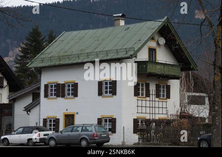 Germany, Munich. A white house with a green roof sits on a suburban street. Two cars are parked in the driveway, hinting at a potential real estate li Stock Photo