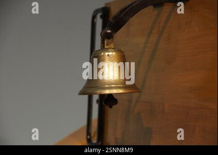 In Germany, Munich, a close-up of a shiny brass ship's bell mounted on a weathered wooden wall. This nautical relic symbolizes both maritime tradition Stock Photo