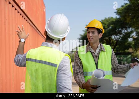 Engineers reviewing construction plans in a logistics environment, focusing on container management. Stock Photo