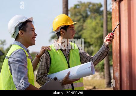 Engineers collaborating on construction plans outdoors with blueprints and communication devices. Stock Photo