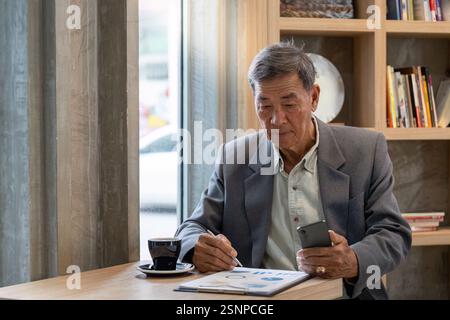 Senior businessman analyzing documents on a tablet while sipping coffee in a contemporary cafe. Stock Photo