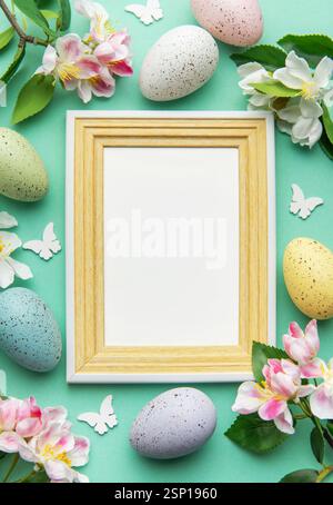 Easter eggs, spring flowers, butterflies, and a blank frame create a festive border on a turquoise background Stock Photo
