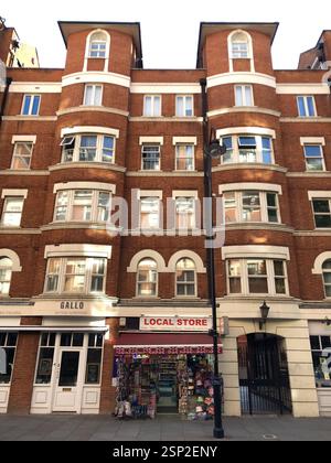 London, England - 10 July 2023, A Small Convenience Store on the Side of an Orange-Colored Building in English Style, Easily Accessible for Passersby Stock Photo