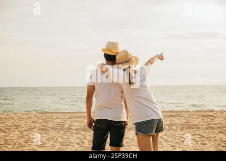 Back Asian couple standing hugging together on the beach, Happy young woman embracing her boyfriend Stock Photo