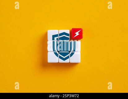 Toy cubes forming a shield symbol being attacked by a lightning bolt cube placed on a yellow background, representing cybersecurity concepts Stock Photo
