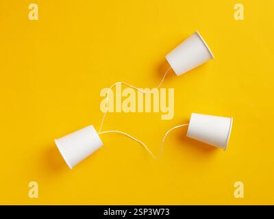 Simple communication device made with two white paper cups and string transmitting sound waves on a vibrant yellow background Stock Photo