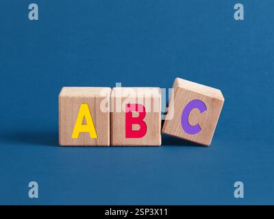 Colorful letters abc are written on wooden cubes, with the letter c falling down, representing early childhood education and learning Stock Photo