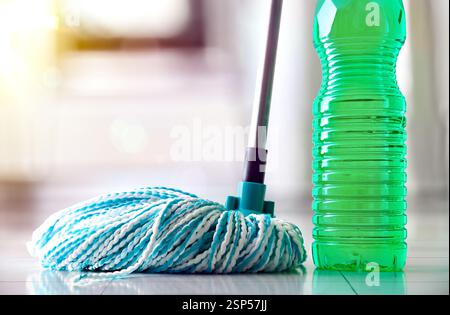 Plastic bottle with green disinfectant product for floor and mop with white and blue fiber strips reflected on white tiled tiles and background cookin Stock Photo