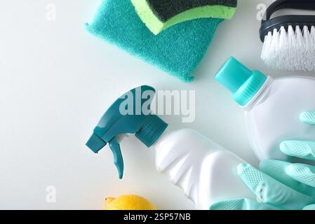 Cleaning products in green tones such as disinfectant, scouring pads, gloves and brush on a white bench and isolated background. Top view. Stock Photo