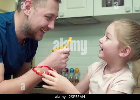 Father and daughter spending time together playing with vegetables in the kitchen Stock Photo