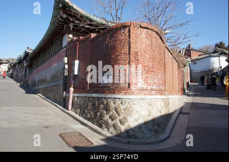 Street scene in South Korea with traditional Korean architecture. Brick wall with curved roof and tiled eaves. Stone wall base. People walking uphill Stock Photo