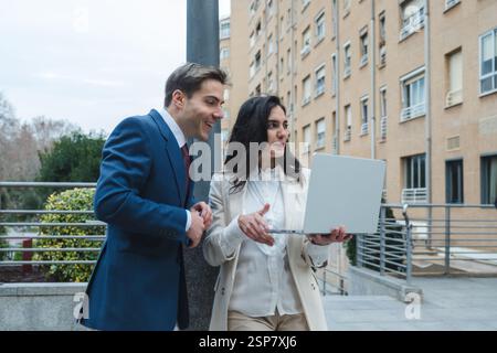 Businessman and businesswoman smiling and using laptop outdoors Stock Photo