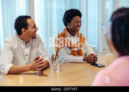 A group of joyful colleagues are seen sharing laughter and positive energy during a meeting. The atmosphere is relaxed with, bright smiles and open co Stock Photo