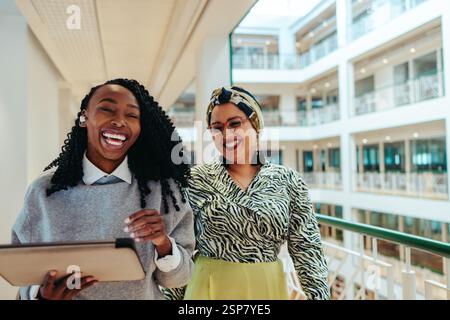 Two coworkers walking through an office building while laughing and enjoying each other's company. The ambiance is lively and friendly, capturing a po Stock Photo