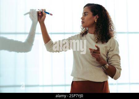 A professional woman writing on a whiteboard, focused on illustrating ideas. The atmosphere conveys concentration and creativity in a modern work envi Stock Photo