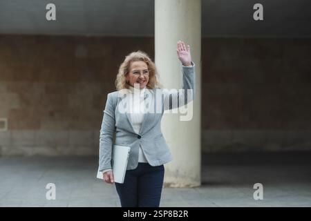 Confident businesswoman waving while walking outdoors Stock Photo
