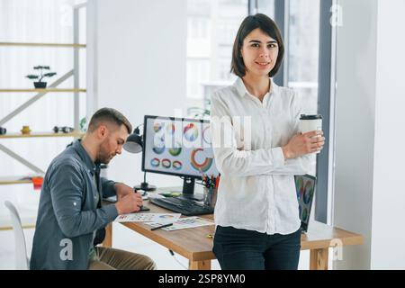 Woman standing in front of man that sitting by the table. Two designers working together in the office. Stock Photo
