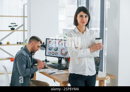 Woman standing in front of man that sitting by the table. Two designers working together in the office. Stock Photo