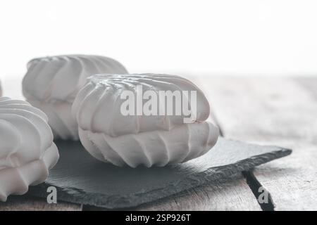 White marshmallows on black slate plate on wooden table Stock Photo