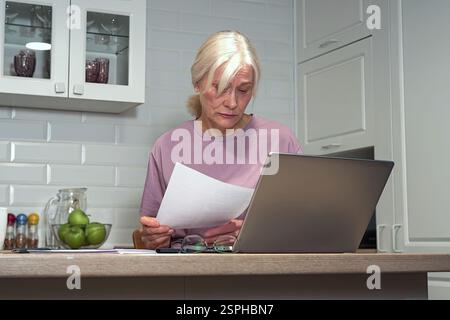 An elderly woman checks documents in the kitchen Stock Photo