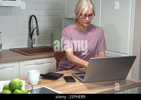 Elderly woman typing on laptop and calculator Stock Photo