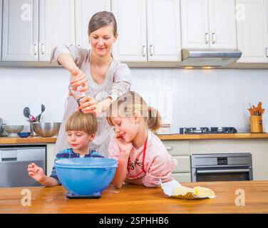 A happy family moment as a mother helps her children bake in the kitchen, fostering teamwork and fun. The scene showcases love, education, and the joy Stock Photo