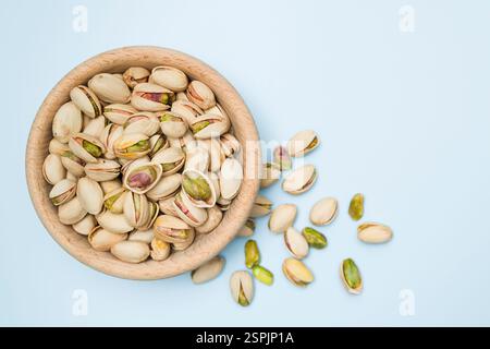 Pistachio nuts into wooden bowl on light blue background. Top view. Stock Photo
