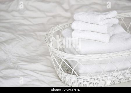 Clean white towels folded in a basket on top of bed Stock Photo
