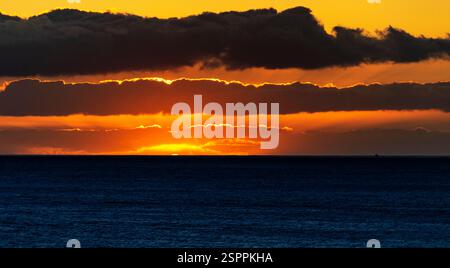 A stunning sunset over the ocean, with vibrant orange and yellow hues illuminating the horizon. Dark clouds frame the scene, creating a dramatic contr Stock Photo
