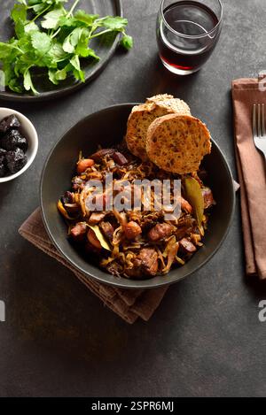 Polish bigos in bowl on dark stone background. Stewed cabbage with sauerkraut, mushrooms, smoked meats and spices. Stock Photo