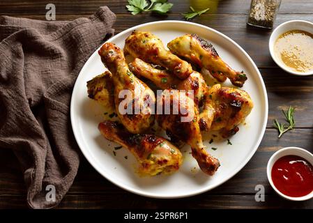 Barbecue roasted chicken drumsticks served with sauce on brown wooden table. Close up view Stock Photo