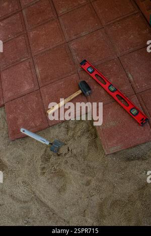 Using a trowel, rubber mallet and a level to build a walkway with red pavers. Stock Photo