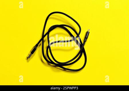 Black usb iPhone charging cable, coiled in a ring, on a yellow background. Stock Photo