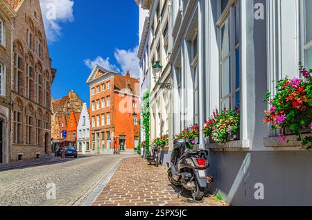 Scooter moped parked on sidewalk of empty cobblestone street, paving stone road, old colorful buildings in Bruges Brugge old town historic city centre Stock Photo