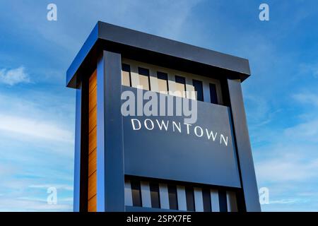 Modern downtown signage featuring white lettering against a dark gray background, set against a vibrant blue sky with wispy clouds Stock Photo